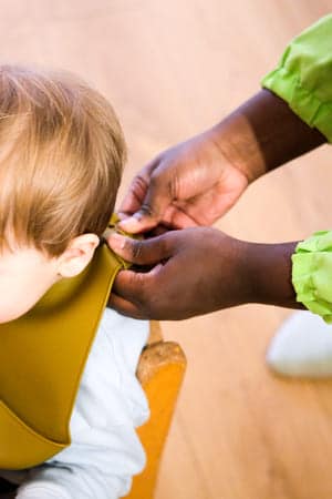 Photo d'une accueillante qui met le bavoir à un enfant